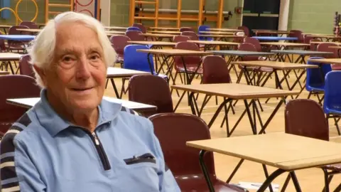 Derek Skipper sitting in a school hall