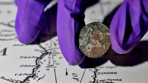 PA Media Diana Davis, Head of Conservation at the National Museum of the Royal Navy, holds a 127-year-old farthing on the gun deck of HMS Victory