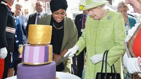 PA Media Queen Elizabeth II cuts the cake Nadiya baked for her 90th birthday