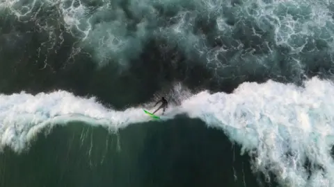 Cem Ozdel/Getty Images An aerial view of a surfer surfing among the giant waves of Atlantic Ocean in Dakar, Senegal on May 25, 2024. In Senegal, which has 724 kilometres of coastline, surf schools with large and small beaches along the coastline are flooded by surfing enthusiasts. Surfers gather at the beach at noon enjoy the sea until the evening hours as the waves grow.