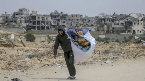 EPA A displaced Palestinian man carries his belongings while walking along a street in Khan Younis, in the southern Gaza Strip (24 March 2024)