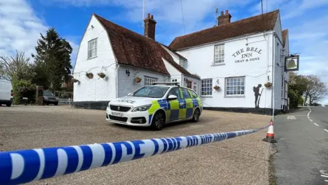 Stuart Woodward/BBC The Bell Inn pub in Feering, near Colchester. An Essex Police car is parked at the pub and a police cordon has been put in place