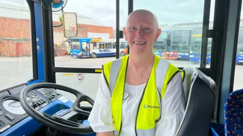 Lady smiles sat in a bus driver's seat