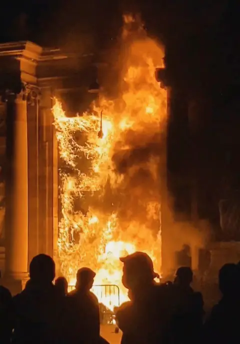 Twitter Bookee0/via REUTERS People look at the Bordeaux town hall in flames during a demonstration as part of the ninth day of nationwide strikes and protests against the French government's pension reform, in Bordeaux, France, March 23, 2023, in this screengrab obtained from a social media video.