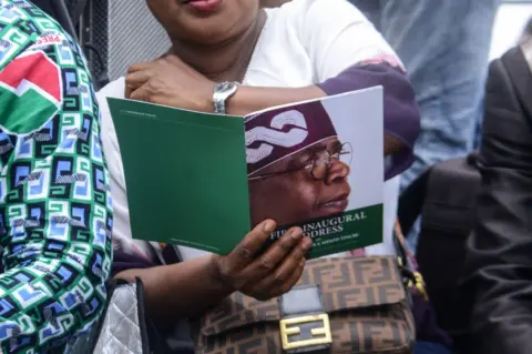 Olukayode Jaiyeola/Getty Images A woman looks at an official booklet showing the face of Bola Tinubu at his inauguration ceremony in Abuja, Nigeria - Monday 29 May 2023