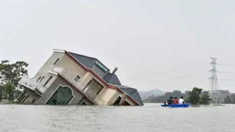 AFP This photo taken on 15 July 2020 shows residents riding a boat past a damaged and flood-affected house near the Poyang Lake due to torrential rains in Poyang county, Shangrao city in China's central Jiangxi province