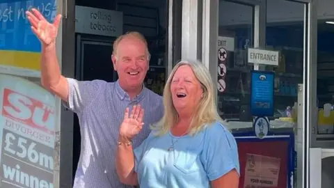 Clive and Angela Mortimer Clive and Angela Mortimer outside Yatton News. They are both waving to the camera and smiling