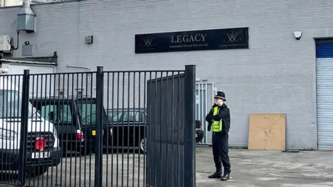 PA Media/Dave Higgens Policeman standing inside Legacy Independent Funeral Directors gated compound