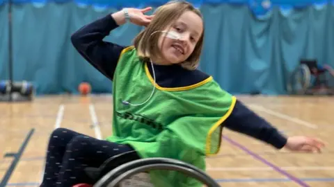 Family photo Imogen in a gymnasium in her wheelchair