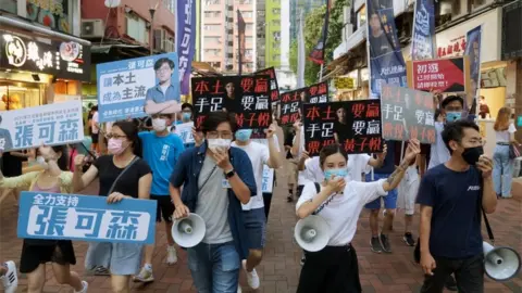 Retuers Sam Cheung Ho-sum and Prince Wong Ji-yuet march on a street to campaign for the unofficial "primary" election organised by the pro-democracy camp, in Hong Kong