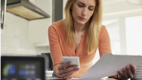 Getty Images Woman looking at bills with calculator
