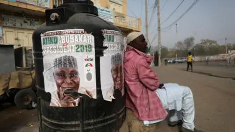 Reuters A man sits next to a campaign poster of Atiku Abubakar, leader of the People"s Democratic Party (PDP), after the postponement of the presidential election in Kano, Nigeria February 17, 2019. REUTERS/Luc Gnago