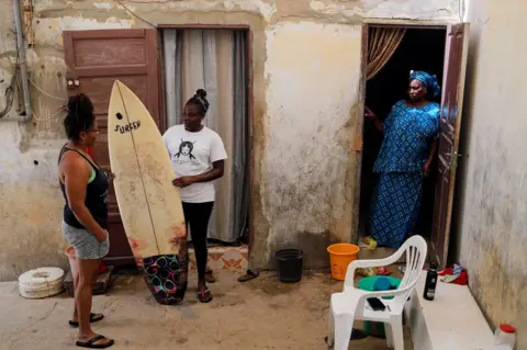 Zohra Bensemra / Reuters Khadjou Sambe stands with her surboard as she talks to her coach Rhonda Harper as her mother looks on