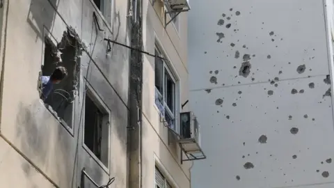 EPA A man looks at the damage caused by a Palestinian rocket that hit a block of flats in the southern Israeli city of Ashkelon (11 May 2021)