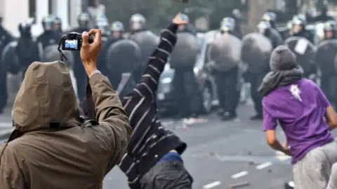 Getty Images Rioters throw objects at riot police in London