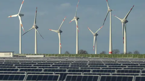 Getty Images Wind turbines behind a solar power plant