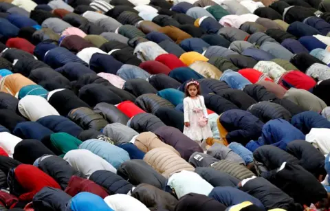 Robert Ghement / EPA-EFE A girl stands and looks aside as worshipers pray while marking Eid al-Fitr at Dinamo Sports Hall, in Bucharest, Romania