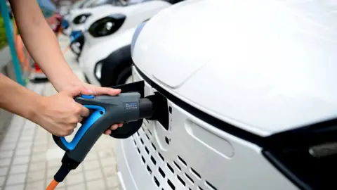 Reuters A staff member hooks up a charging cable to an electric vehicle