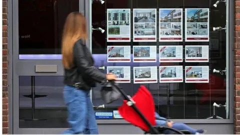 AFP Woman with pram walks past estate agents