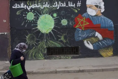 EPA A woman wearing a mask walks past a large mural depicting a masked health worker cradling the nation of Morocco in their arms.