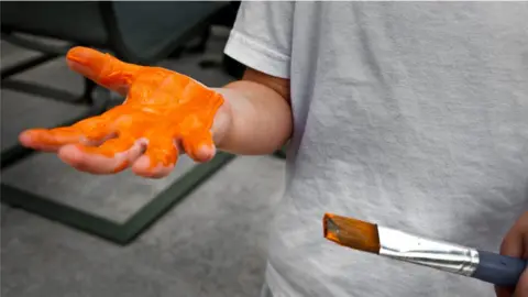 Getty Images Boy with orange paint on one hand and holding a paint brush with another