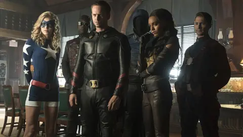 The CW Network Legends of Tomorrow actors: (L-R): Sarah Grey as Stargirl, Kwesi Ameyaw as Dr Mid-Nite, Patrick J Adams as Hourman, Dan Payne as Obsidian, Maisie Richardson-Sellers as Amaya Jiwe/Vixen and Matthew MacCaull as Commander Steel