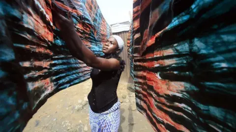 EPA A woman hangs dyed textiles in Adjame, Abidjan, Ivory Coast, 22 January 2018.