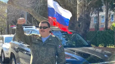 Aussie Cossack Simeon Boikov, known online as Aussie Cossack, raising first in front of Russian flag