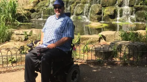 Dan Dorszynski Dan sitting in his powerchair in front of a waterfall