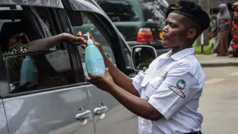 AFP A security officer dispenses chlorinated water to a passenger at Muhimbili National Hospital in Dar es Salaam