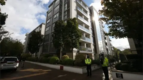 PA Media Police officers stand outside a block of flats where a boy and two adults died
