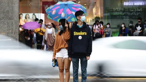 Getty Images A couple wearing protective masks wait to cross a street in the rain on 10 January 2021 in Singapore