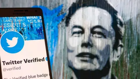 Getty Images Twitter Verified icon seen on mobile screen with Elon Musk in a background illustration.