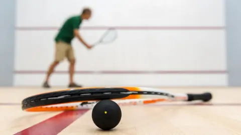 Getty Images Squash player, racket and 1-spot ball lying on the floor of an empty squash court