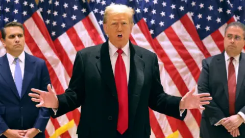 Getty Images Donald Trump, flanked by his lawyers, holds a press conference after a judge scheduled his criminal hush money trial to begin on 15 April.