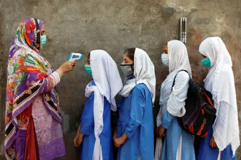 Fayaz Aziz / Reuters Students wear protective face masks as they have their temperature checked before entering a class in Peshawar, Pakistan 23 September 2020