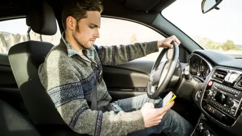 Getty Images A man looking at his phone while driving