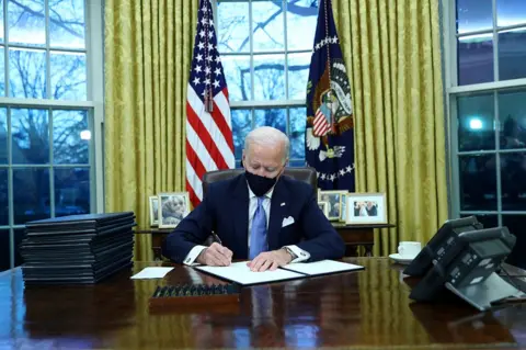 Reuters US President Joe Biden signs executive orders in the Oval Office of the White House in Washington, after his inauguration as the 46th President of the United States, 20 January 2021.