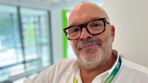 Image of Tim Weston, a man wearing glasses and a green lanyard