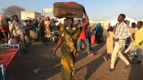 Hassan Lali/ BBC Woman carrying a suitcase on her head