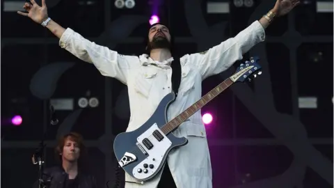 Getty Images Serge from Kasabian performs on stage with his arms held out to his side