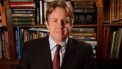 Getty Images Marcus Fysh sitting down with a bookshelf in the background