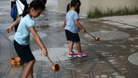 Getty Images Japanese girls splash water on the ground during a water sprinkling event called Uchimizu which is meant to cool down the area, in Tokyo on July 23, 2018.