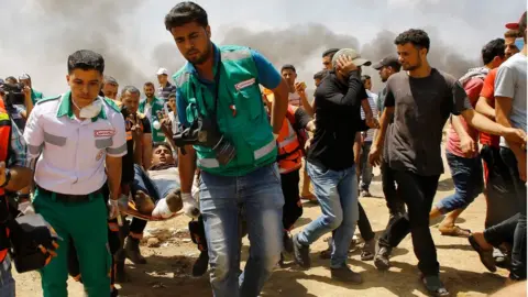 AFP Emergency services and Palestinians carry a wounded protestor during clashes with Israeli security forces near the border between Israel and the Gaza Strip, east of Jabalia on May 14, 2018