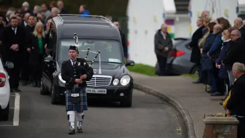 PA Media A piper plays as the hearse carrying Mr McGill, arrives at St Michael's Church for his funeral Mass