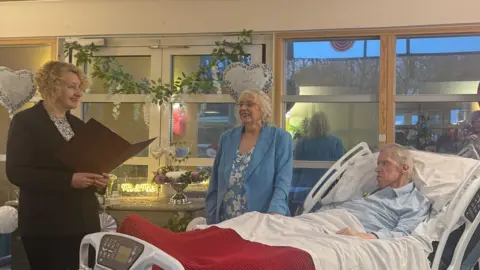LOROS A registrar carrying out a wedding ceremony for a woman in a blue dress and a man in a hospital bed