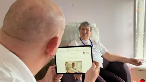 A man is holding a tablet computer and recording a woman as she looks at him