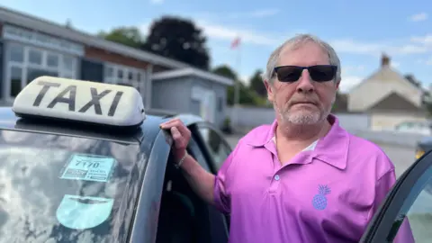 BBC Steve Mackie stood next to his taxi with the door open