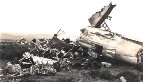 Clee Hill Flying Fortress Crash Memorial Fund A black and white image of a plane crash. The plane is lying on grass in bits, with metal and wreckage strewn around