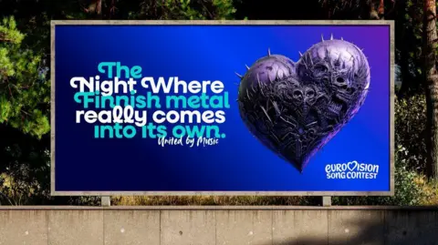 PALS/EBU A roadside billboard. The poster is blue and shows an image of a heart made from spikes and skulls. A caption says 'The night where Finnish metal really comes into its own. United by Music. Eurovision Song Contest'.